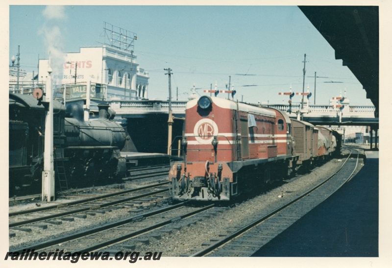 P18412
Ex-MRWA F class 41, in MRWA livery, on goods train, steam loco on adjacent track, bracket signals, road bridge, Perth station
