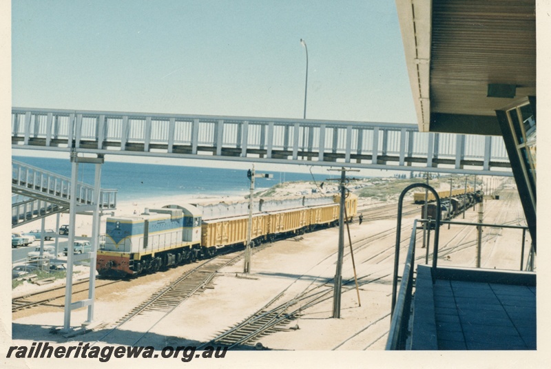 P18434
J class diesel on wheat train comprising WG class wagons modified to carry grain, signal, overhead footbridge, beach, Leighton yard, ER line, front and side view
