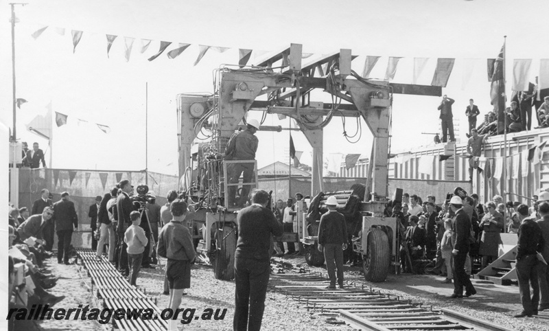 P18480
11 of 12 images relating to the ceremony for the linking of the standard gauge railways at Kalgoorlie, last 30 foot section of track linking the standard gauge railways is laid, track laying machine, seated guests and spectators look on
