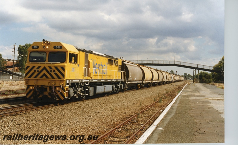 P18660
Q class 301 standard gauge diesel locomotive hauling an empty grain train eastbound through Midland. Locomotive painted in Westrail yellow and portion of overhead footbridge in background. ER line.
