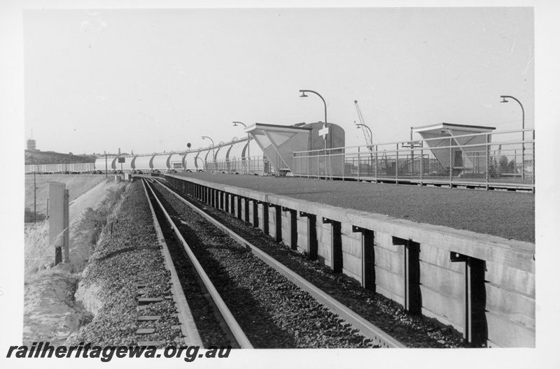 P18708
Station platform, station nameboard, platform lights, end of passing goods train, passenger shelters, North Fremantle, ER line 
