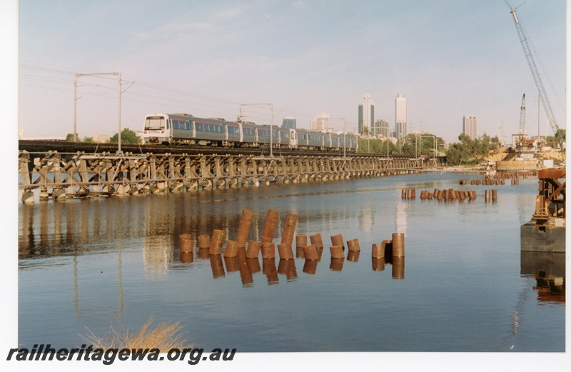 P18719
A four car EMU set crossing the old Bunbury Rail bridge at East Perth enroute to Perth. Construction of the new Goongoongup bridge is in progress. 
