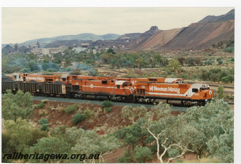 P18760
Mount Newman (MNM) M636 class 5477, 5467 depart Newman with loaded ore train bound for Port Hedland. Mount Whaleback in background. 

