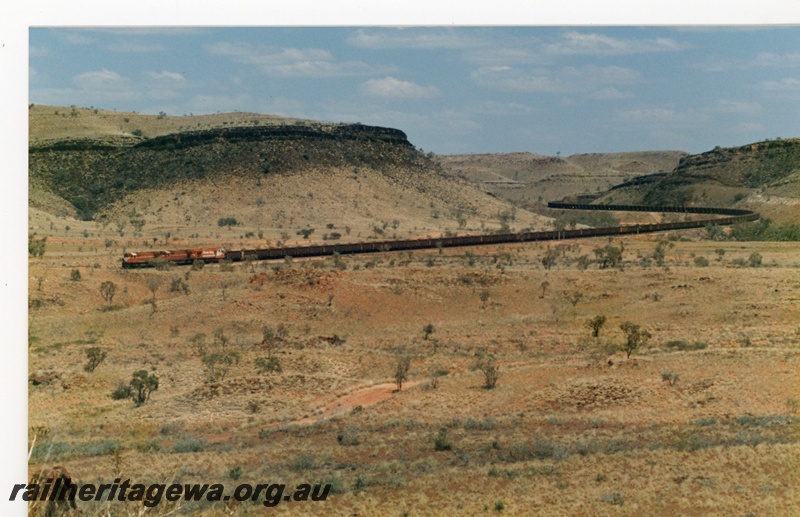 P18766
Mount Newman (MNM) a triple headed loaded ore train snakes through the Chichester Ranges near Garden siding.
