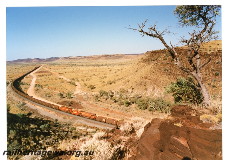 P18795
Mount Newman (MNM) Locotrol locomotives in centre of loaded ore train near Garden. Chichester Ranges in background.
