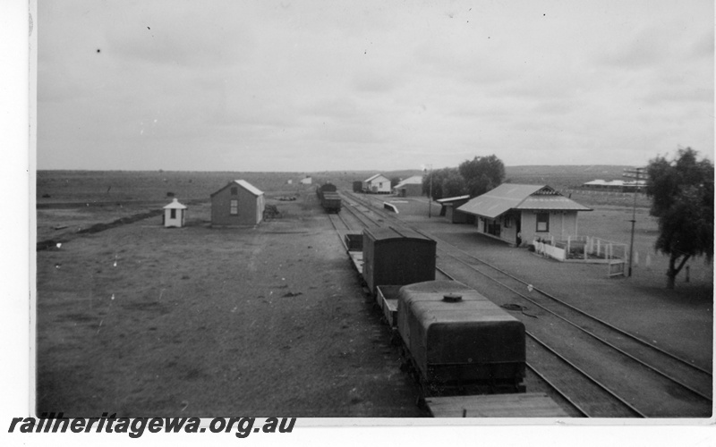 P19016
Overview of Tarcoola station, wagons in siding including tank wagon bringing water from Port Augusta with round lid in foreground, bakehouse on left side of tracks, station building, loading ramp, other buildings, Tarcoola, South Australia, TAR line
