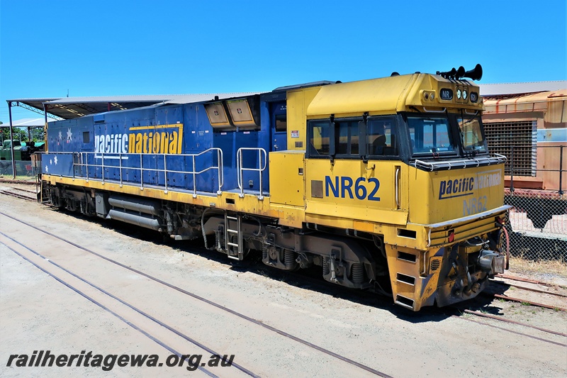 P19558
Pacific National NR class 62 in the blue and yellow livery passing through the site of the Rail Transport Museum, Bassendean, side and front view
