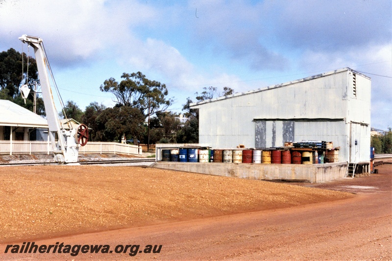 P19590
Platform crane, goods shed, loading platform, Goomalling, EM line, trackside and end view of the shed, note the 44 gallon drums at the side of the shed.
