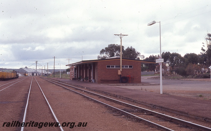 P19763
Station building, station nameboard on light, rake of wagons, wheat bins, loaders, track, Wongan Hills, EM line
