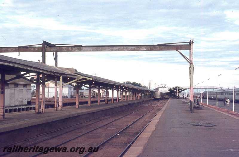 P19799
Main platform, dock platforms, canopies, station building, passenger train at station, people on platform, loading beam, goods shed, pedestrian footbridge, Kalgoorlie, TAR line
