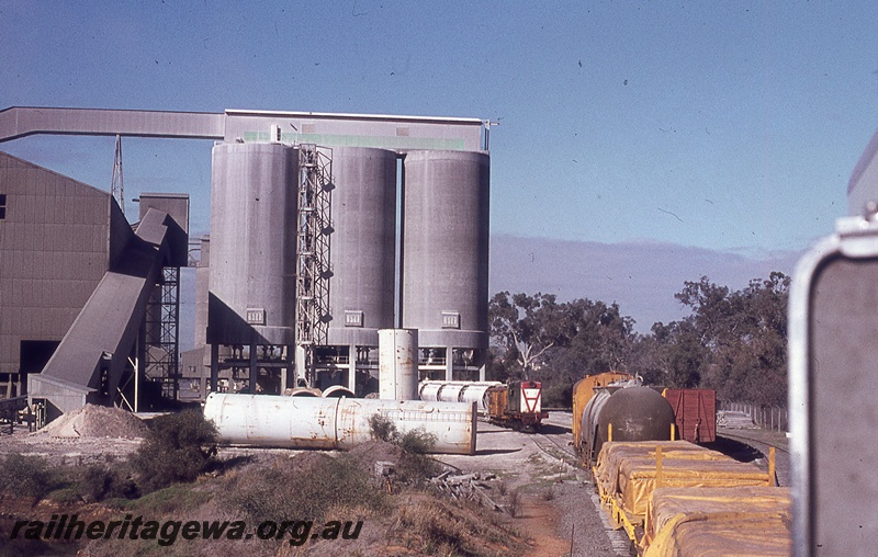 P19812
Y class diesel, on train of van and hoppers being loaded, rake of van, tanker and flat wagons, silos, elevator, conveyor, Soundcem, middle distance view
