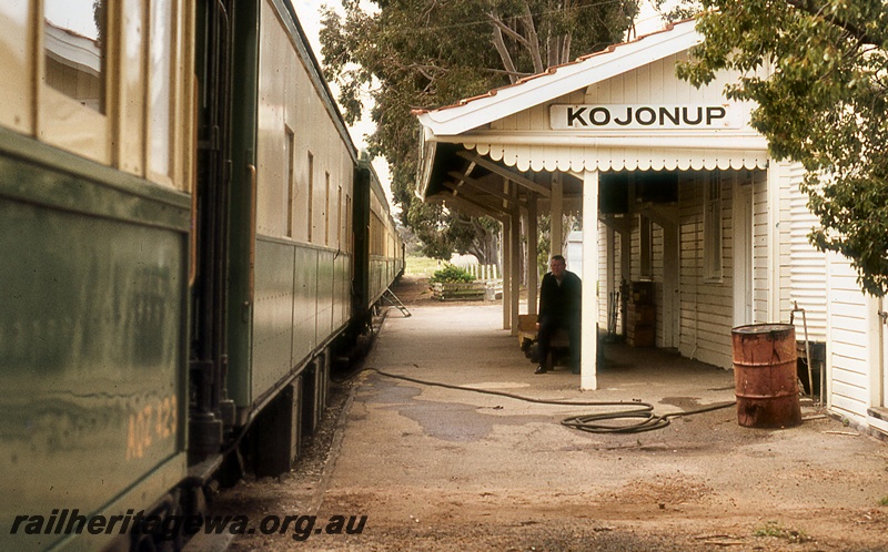 P19936
AQZ class 123 carriage, in train of other carriages, standing at station, station building, station attendant, station nameboard, Kojonup, DK line
