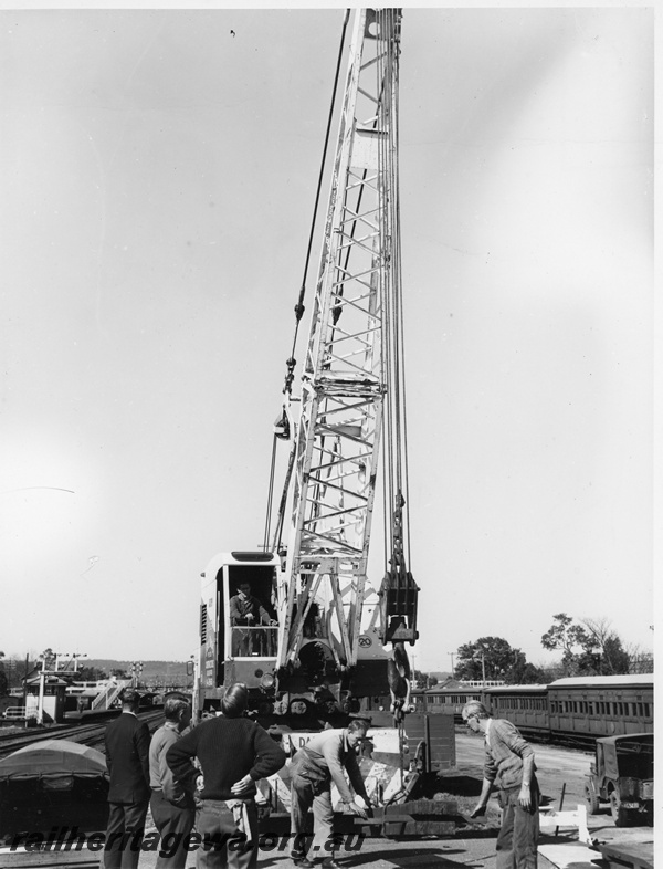 P20277
Goods despatch to the South West flood zone, No 2 of 3, signal box, bracket signals, Bell Bros mobile crane loading materials, workers, carriages, Midland, ER line, front view of crane
