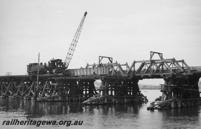 P20390
Unidentified K class attached to steam-operated railway crane positioning new girder for repair of Fremantle railway bridge after flood damage of 1926. ER line.
