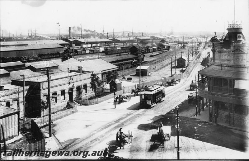 P20460
Brill tramcar No. 3 opposite the original Fremantle railway station, station building, goods yard, warehouses, ship funnels and masts, overhead footbridge, horse drawn carts, His Majesty's hotel building, trackside sheds, tracks, Mouat Street, Fremantle, ER line, view from elevated position, c1906, (similar to P21480)
