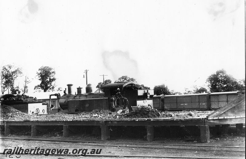 P20484
QA class 142, taking on coal, workers filling coal baskets, vans including Loco Dept V class 3307, wooden platform, water crane, building, side and rear view, c1915
