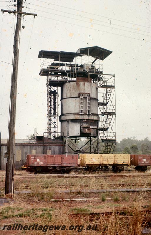 P21059
2 of 3 views of the cylindrical steel coal stage at Collie, BN line, trackside view of the whole structure, Wagons GST class 6424 in the brown livery and GC class 6906 in the yellow livery on the line in front of the structure
