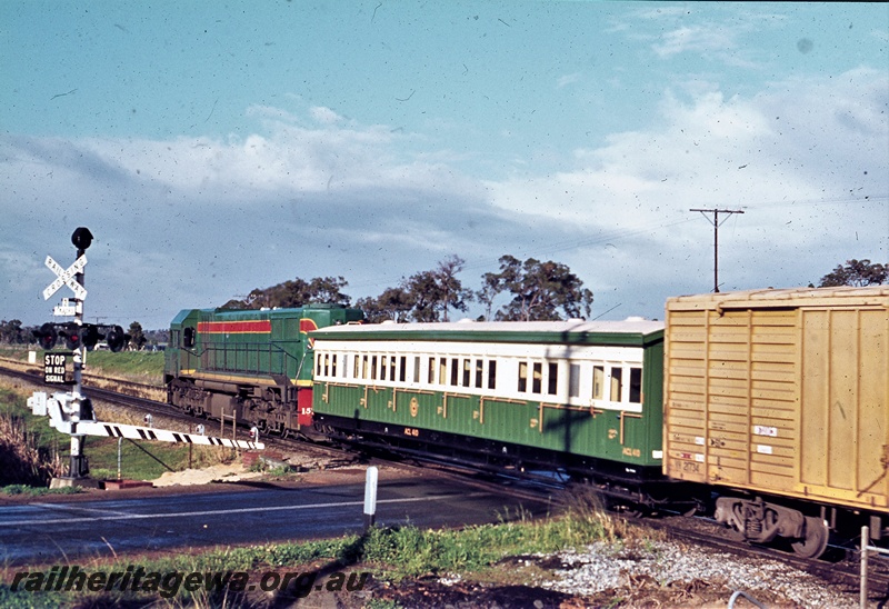 P21189
WAGR DA class 1574 in the green with red and yellow strips livery hauling a short goods train southwards crossing the  West Parade level crossing,  Hazelmere with ACL class 401 carriage in the consist
