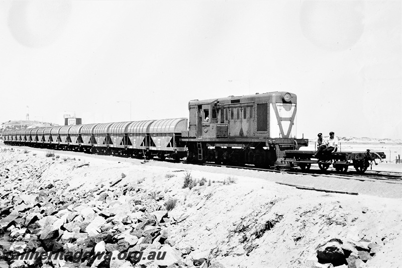 P21282
Y class 1102, hauling wheat wagons to Bunbury jetty, with shunters float with two workers seated on it in front of the loco, breakwater, BP terminal in the background, Bunbury, SWR line, side and front view
