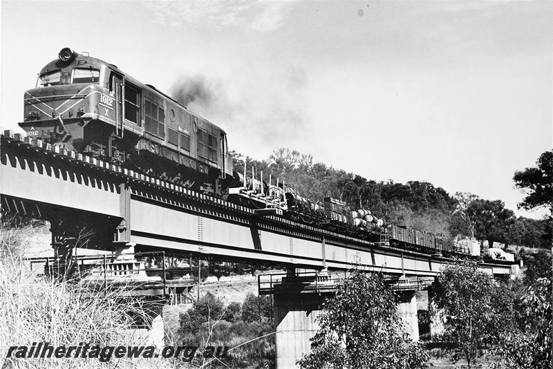 P21289
X class 1012 hauling goods train including flat wagons with bolsters, vans, other wagons, on concrete and steel bridge, Bridgetown, PP line, front and side view from below bridge level
