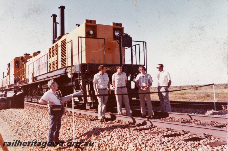 P21322
Loram Australian Rail Service rail grinder, on tracks, four men standing on tracks in front of the grinder, sound technician, ribbon across tracks, Port Hedland, side and end view from trackside
