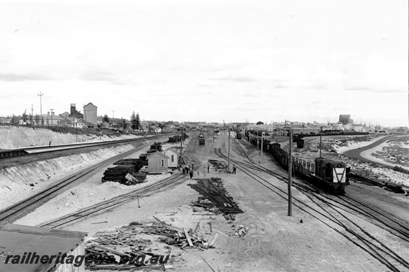 P21332
Construction of  yardmaster's office and Control Tower,  Y class diesel on goods train, trackwork being laid, workers, trackside buildings, Fremantle port in background, Leighton, ER line, view from elevated position
