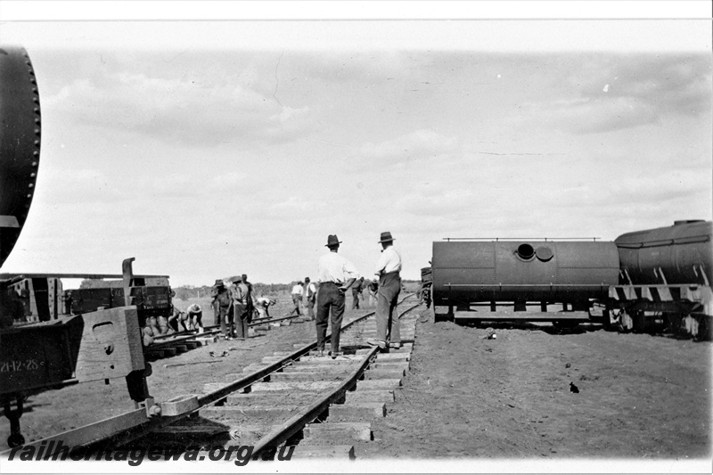 P21374
Derailment of permanent way train, wagons off track, twisted rails, repairs under way by workers, supervisors, construction of Meekatharra to Wiluna section, NR line, c1929-1931
