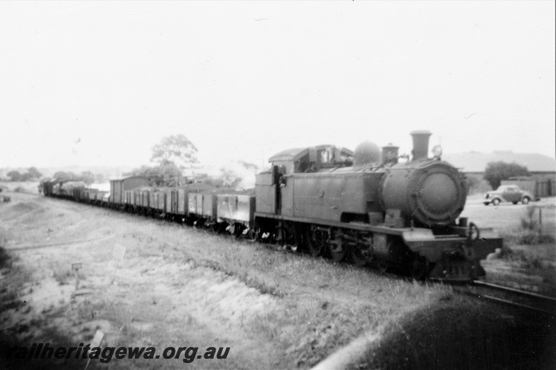 P21394
DS class loco on goods train, passing up Rivervale bank, car and building beside track, SWR line, side and front view
