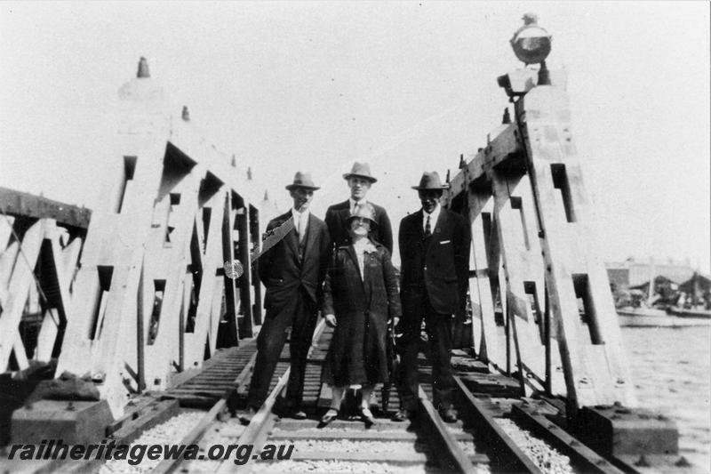 P21473
Wood trestle rail bridge over Swan River, reopening after rebuilding after washaway, WAGR Ways & Works Superintendent Charles Hoare (rear right) with three other persons, standing on the tracks at the end of the rebuilt bridge, Fremantle, ER line, track level view
