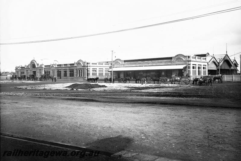 P21476 
Station building, parcels office, horse drawn wagons and carriages drawn up outside, pedestrians, picket fence, roadway, overhead wires, Fremantle, ER line, view from roadway
