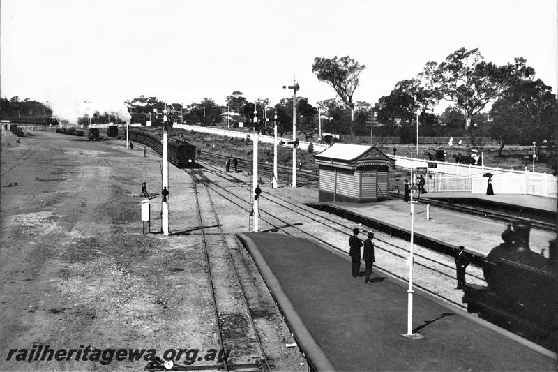 P21481
Steam hauled train, steam loco (front portion), yard, level crossing, points, point lever, signals, bracket signals, tracks, platforms, gentlemen's toilet. picket fence, workers, pedestrians, east end of Claremont station, ER line, elevated view, c1905
