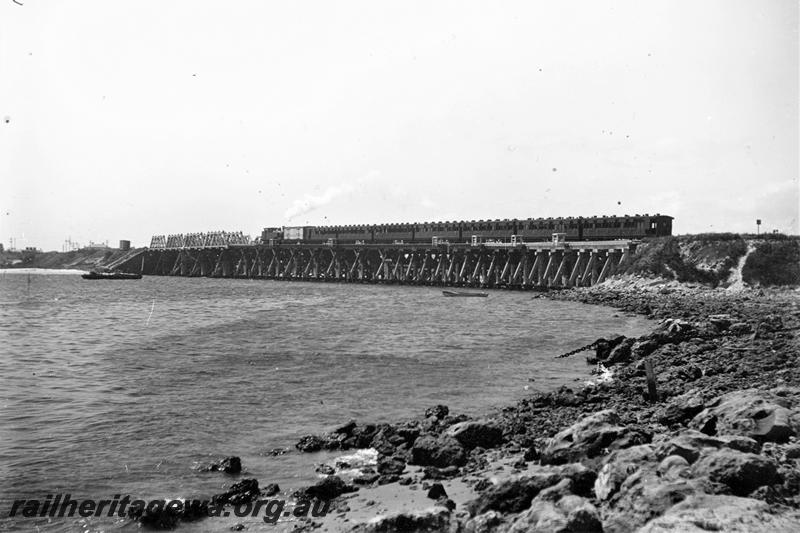 P21482
Steam hauled passenger train, crossing wooden trestle bridge, barge, Swan River, Fremantle, ER line, view from river bank
