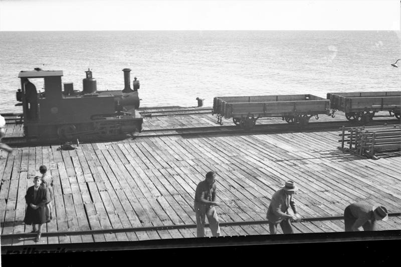 P21503
Tank loco, low sided wagons, men, boys, wooden jetty, ocean, view from elevated position
