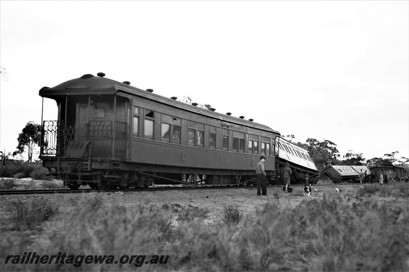 P21512
Passenger train derailment scene, several carriages off track, one carriage with end platform still on rails, onlookers, view from trackside 
