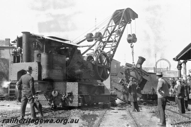 P21513
Scene after collision and derailment of N class 85 and N class 203, railway crane lifting loco, workers, onlookers, overhead footbridge, water column, canopy, tracks, Perth station, ER line, trackside view
