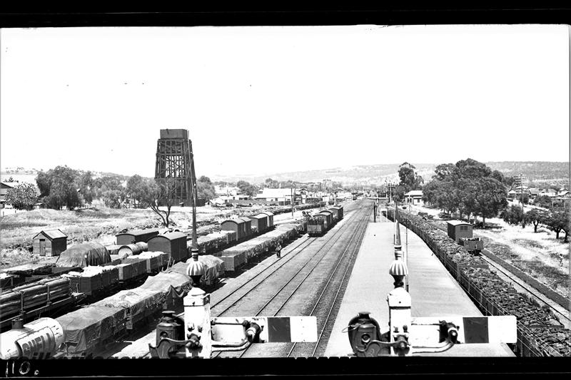 P21517
View of station and yard, trackside sheds, rakes of wagons and vans, platform, water tank, tops of signals, houses in distance, Northam, ER line, elevated view from signal box looking east

