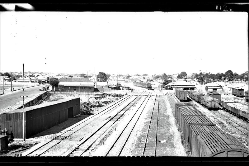 P21519
Steam hauled train No 4, arriving in Northam from East Northam, rake of livestock wagons in right foreground with elephant wagon closest to camera, others rakes of vans and wagons,  road, sheds, level crossing, houses in background, Northam, EGR line, elevated view  
