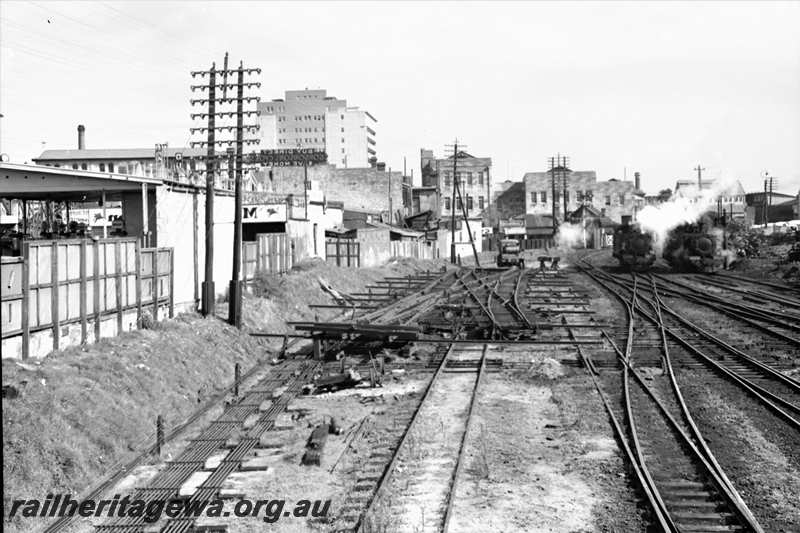 P21615
Scissors crossover assembly, two tank locomotives, pointwork, tracks, telegraph poles, trackside rodding, various buildings, Perth, ER line, view along tracks
