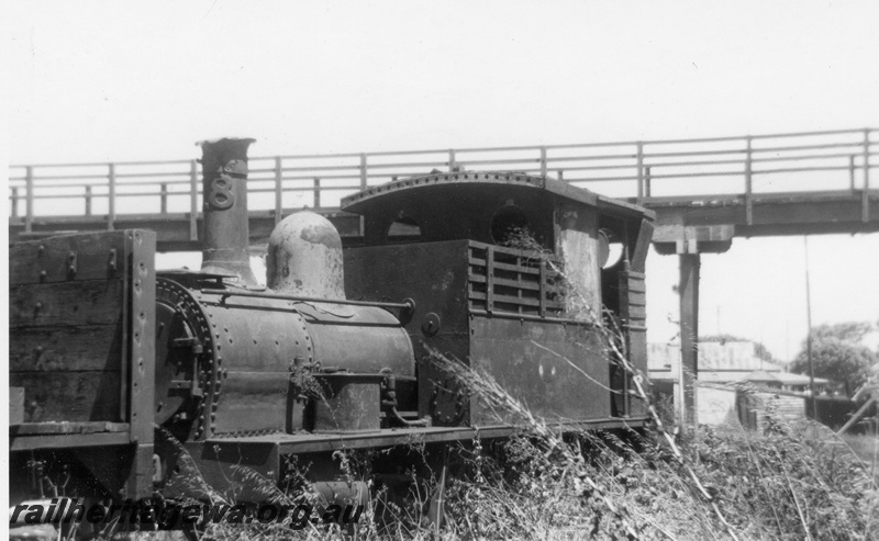 P21863
Former Public Works Department steam loco H class 18, in open storage at loco depot, overhead bridge, Bunbury, SWR line, front and side view
