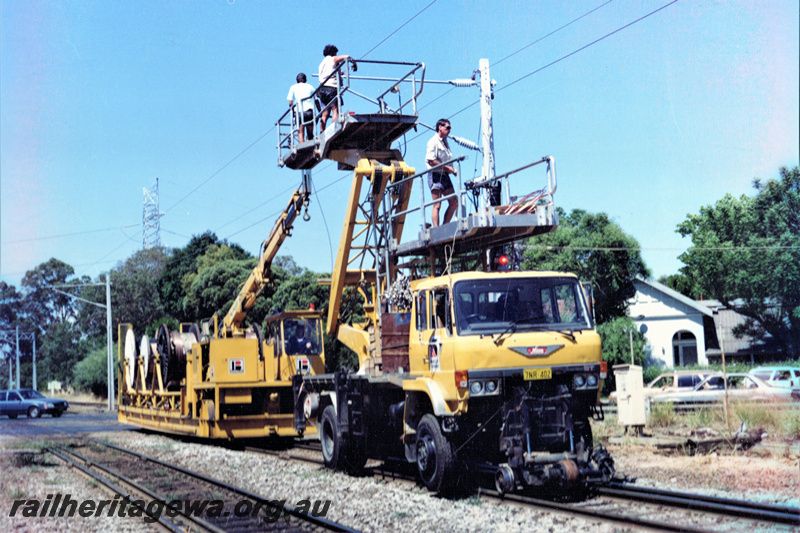 P22035
Installation of overhead electric wires for Perth urban rail network, East Guildford, East Street level crossing, Brown Boveri road-rail truck with cherry picker, Brown Boveri rail crane with electrical cables, men on cherry picker platforms, poles, wires, side and front view from track level
