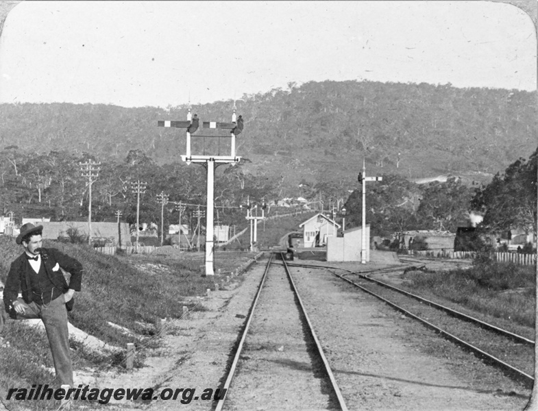 P22162
Station building, platform, bracket signals, signal, bystander, tracks, Bellevue, ER line, view along the tracks toward the station and Darling range, c1900
