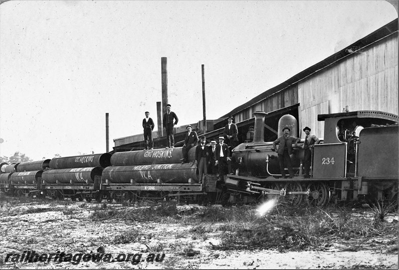 P22164
G class 234, on goods train comprising K class 3245 wagon and other K class wagons, loaded with G&G Hoskins pipes, bystanders, shed, Midland Junction, ER line, side and end view from trackside, c1900
