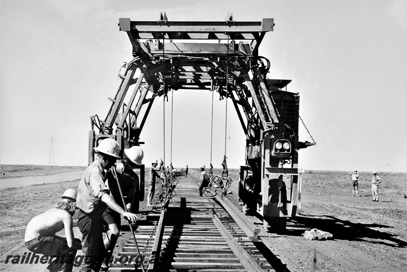 P22203
Track laying machine, workers, rails, sleepers, on construction of the extension of the Goldsworthy Mining Railway to Shay Gap, Pilbara, track level view

