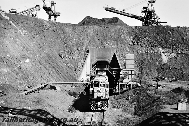 P22208
Mount Newman Mining diesel 5470 on a loaded train emerging from load out tunnel, conveyors, loaders, tunnel portal, pipeline, Mount Newman, Pilbara, front view from elevated position
