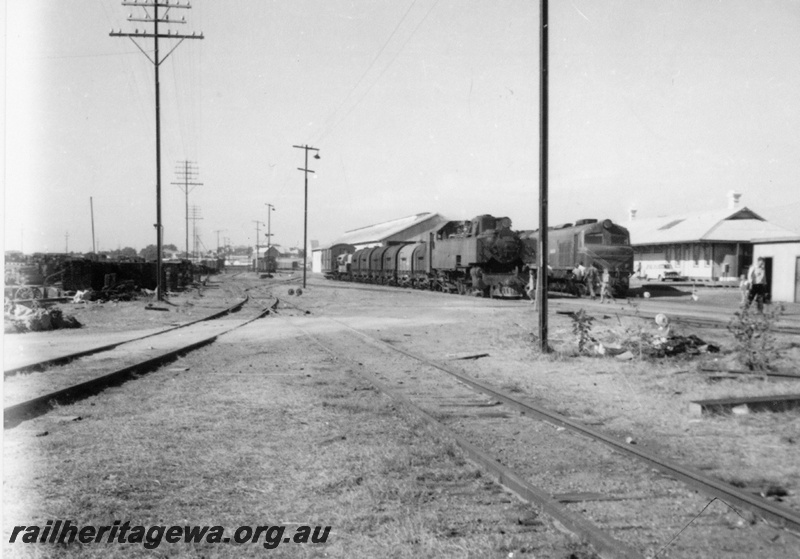 P22269
UT class 664, on goods train including oil tankers, wagon, van,  X class loco, in background offices of District Loco Superintendent, Clerk in Charge (R. Gratte 1935-1966), store and drivers room, yard, tracks, points, Geraldton, NR line, side and front view
