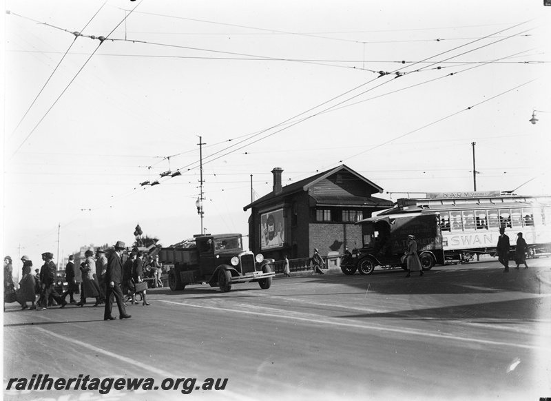 P22344
Electric tram, with advertising signs for NARM Sandshoes and Swan Lager, on Barrack Street bridge, signal box C, motor lorries, pedestrians crossing Wellington Street roadway, overhead electric tram wires, near Perth station, view from roadway
