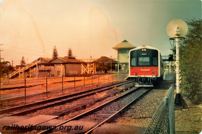 P22359
DMU railcar set, Fremantle bound, pedestrian overpass, goods shed, pedestrian rail crossing, signal box, platforms, back of colour light signal, Claremont, ER line, front and side view 
