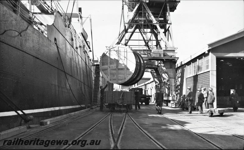 P22380
Loading of vats for Merredin Brewery at Fremantle ER line 2 of 4, vat being lowered onto wagon by crane, ship, wharf, warehouse, onlookers, end view from wharf side
