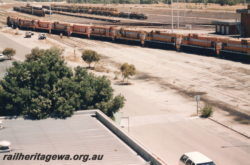 P22424
Lash up of 10 diesel locomotives including A and AB classes, sidings, rakes of wagons, workers, motor vehicles, Forrestfield marshalling yard, ground level view of sides and ends of locomotives
