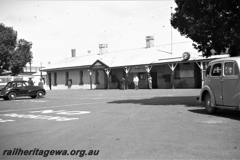 P22429
Station building, clock, carpark, pedestrians, Kalgoorlie, EGR line, view from carpark 
